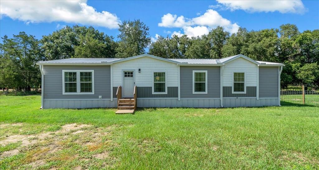 A single-story manufactured home with gray and white siding sits on a grassy lot — 14450 SE SUNSET HARBOR ROAD, WEIRSDALE, FL