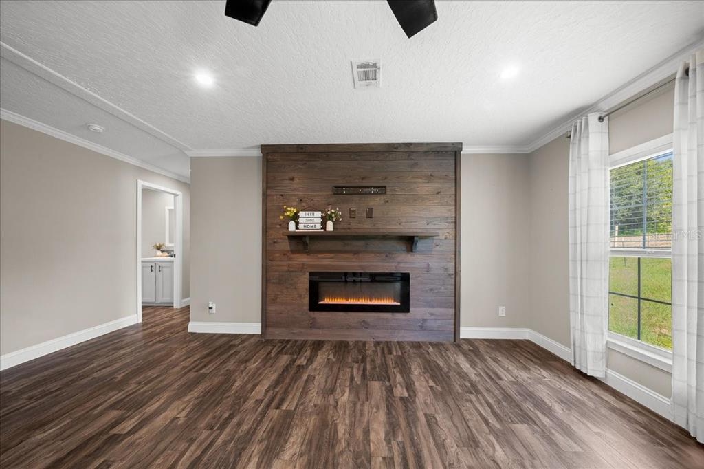 A living room features a wood-paneled fireplace wall, dark wood-look flooring, and a large window — 14450 SE SUNSET HARBOR ROAD, WEIRSDALE, FL