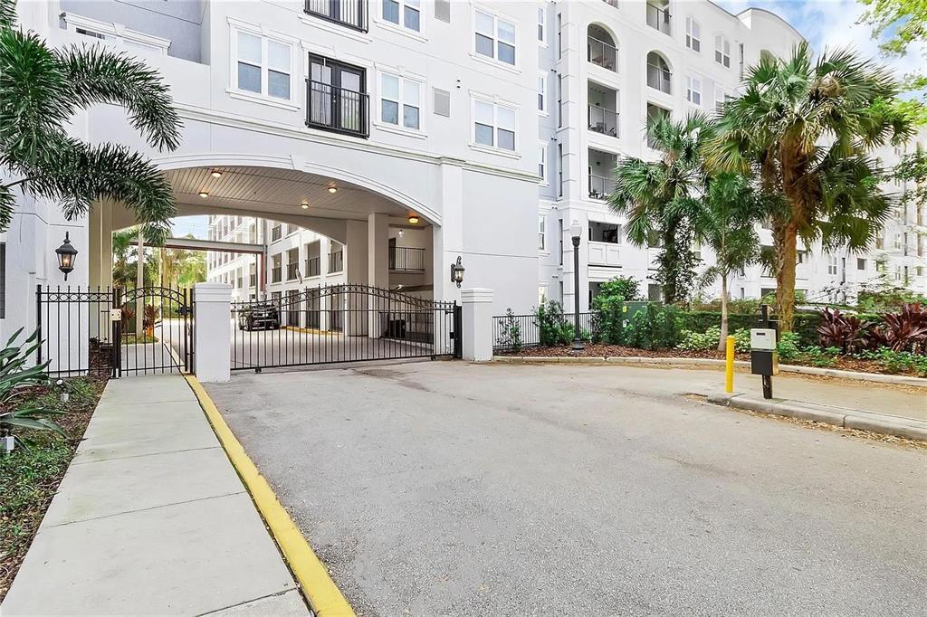 A gated entrance leads to a covered driveway beneath a multi-story white apartment building — 204 SOUTH STREET UNIT 1053, ORLANDO, FL