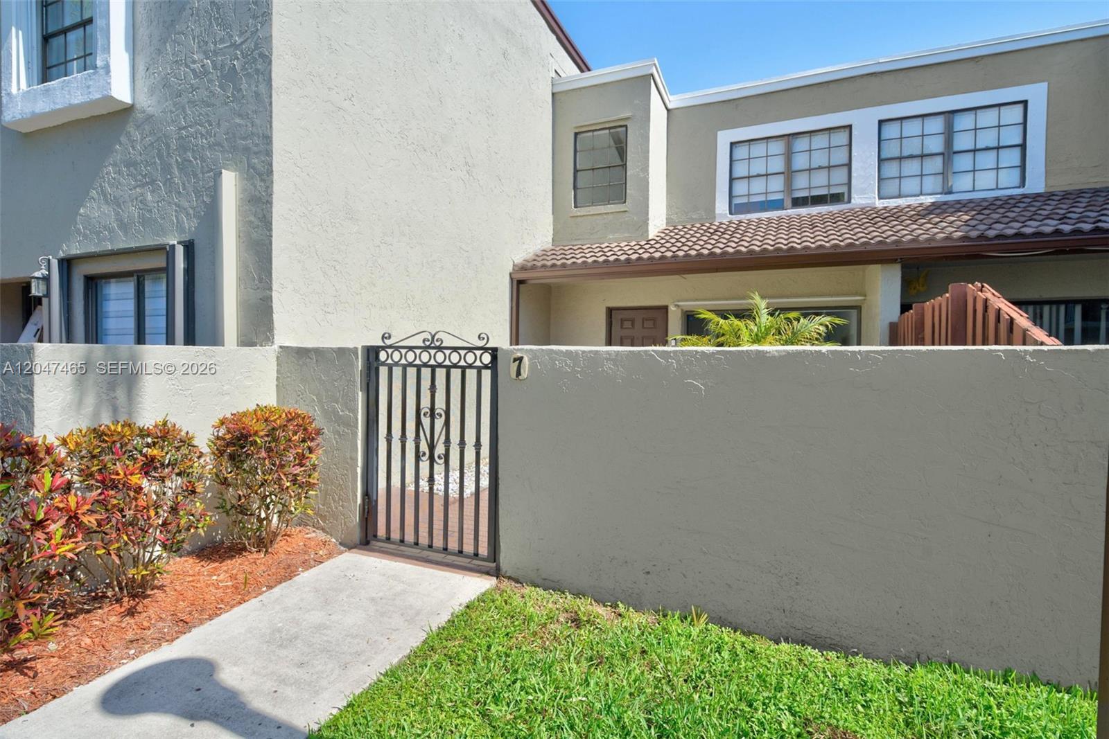 A concrete walkway leads to a gated courtyard entrance of a two-story stucco townhouse — 10505 SW 153rd Ct # 7, Miami FL 33196, MIAMI, FL