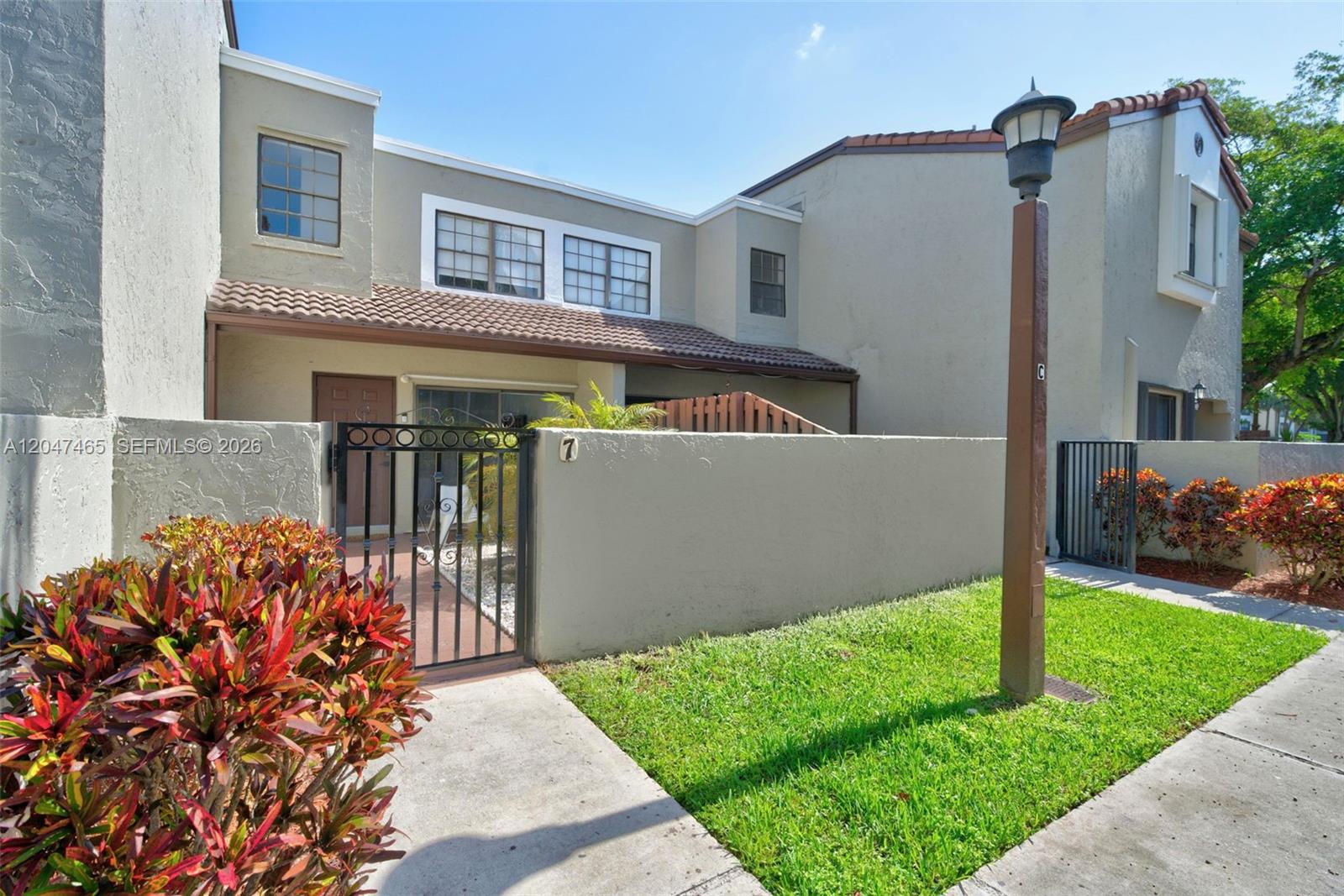A two-story townhouse exterior features a gated courtyard, a stucco facade, and a lamp post — 10505 SW 153rd Ct # 7, Miami FL 33196, MIAMI, FL