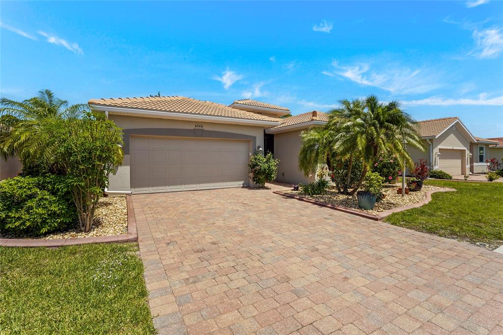 A single-story house with a beige stucco exterior, a tiled roof, and a paved driveway — 6240 FALCON LAIR DRIVE, NORTH PORT, FL