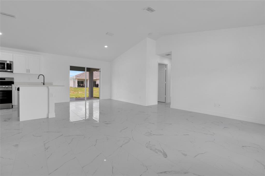 An open-concept kitchen and living area features white cabinetry, marble-look tile flooring, and sliding doors — 1157 NW 7TH AVENUE, CAPE CORAL, FL