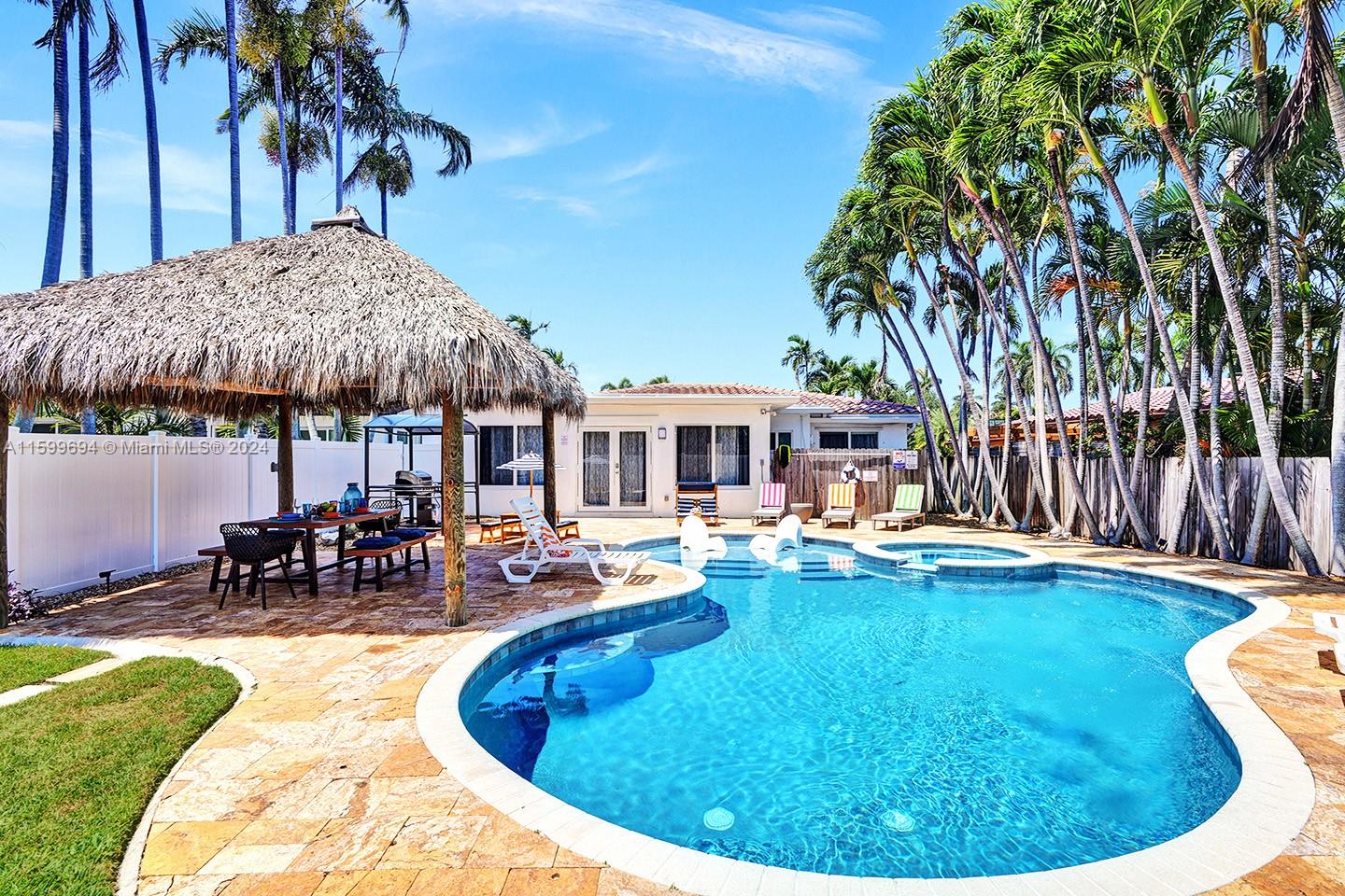 A backyard features a swimming pool, a thatched-roof tiki hut, and several palm trees — 1206 Lincoln St, Hollywood FL 33019, HOLLYWOOD, FL