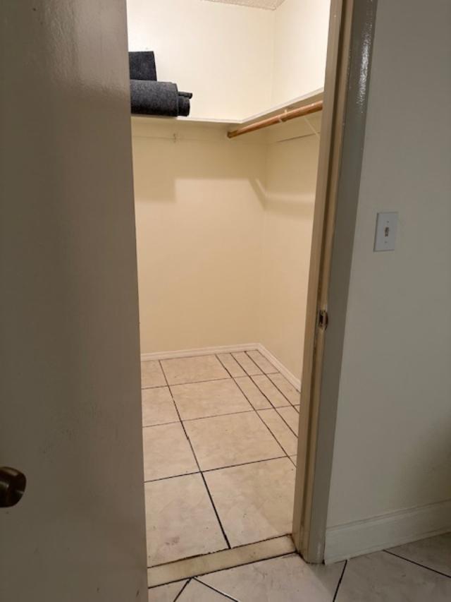 A walk-in closet with beige tile flooring, a white shelf, and a wooden hanging rod — 6505 WINFIELD Boulevard # 14, Margate FL 33063, MARGATE, FL