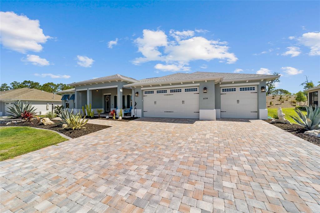 A single-story house with a paved driveway, three-car garage, and desert-style landscaping under a blue sky — 10298 SW 96TH LOOP, OCALA, FL