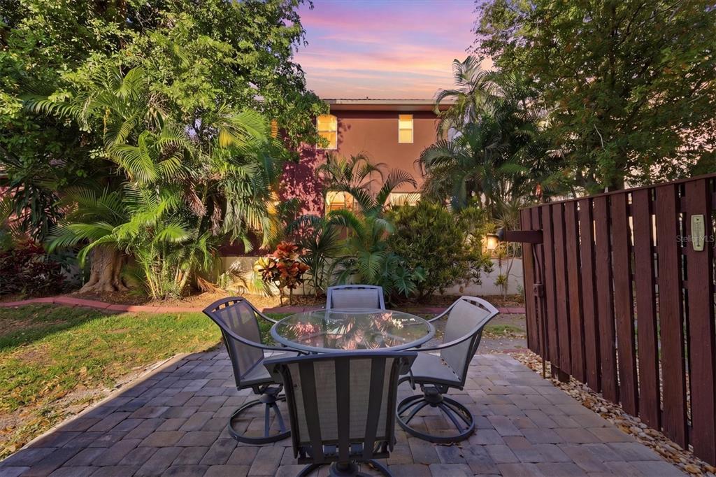 A patio with a glass-topped table and four chairs sits before a house and trees — 260 SANTA MARIA STREET UNIT 105, VENICE, FL