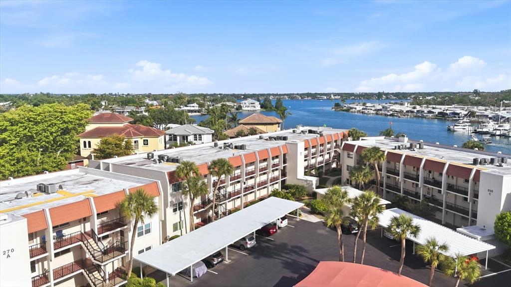 An aerial view shows multi-story apartment buildings with covered parking lots near a waterfront — 260 SANTA MARIA STREET UNIT 105, VENICE, FL