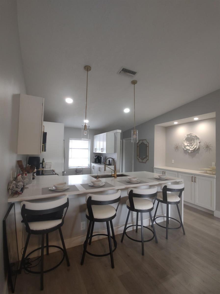 A kitchen features a white island with four bar stools, white cabinetry, and recessed lighting — 18768 Argosy Drive, Boca Raton FL 33496, BOCA RATON, FL