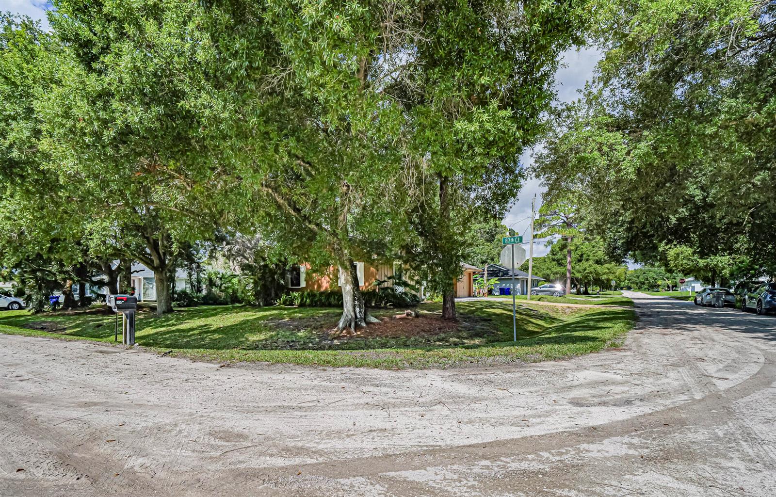 A residential street corner features a house partially obscured by large trees and green lawns — 8745 24th Street, Vero Beach FL 32966, VERO BEACH, FL