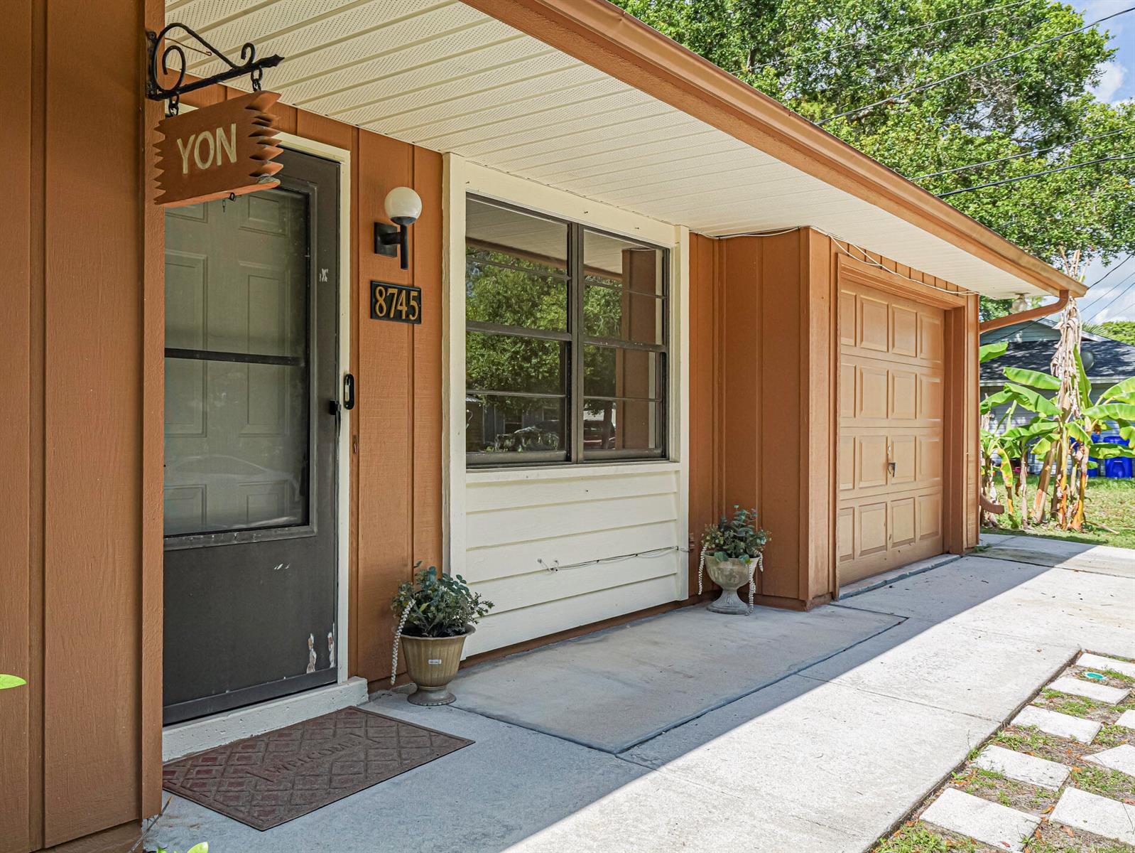 The exterior of a house features a brown front door, a garage, and a window — 8745 24th Street, Vero Beach FL 32966, VERO BEACH, FL
