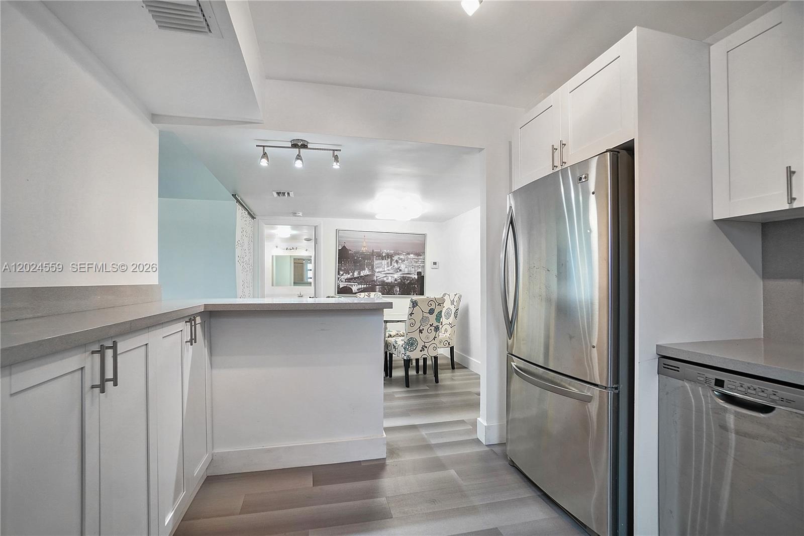A kitchen with white cabinets, stainless steel appliances, and a breakfast bar overlooks a dining area — 9273 Collins Ave # 309, Surfside FL 33154, SURFSIDE, FL