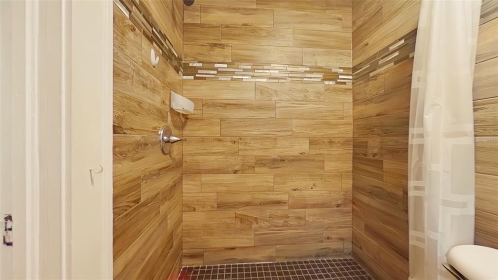 A walk-in shower features wood-look tile walls, a mosaic accent strip, and dark floor tiles — 1412 NW 3RD AVENUE UNIT Upstairs, GAINESVILLE, FL