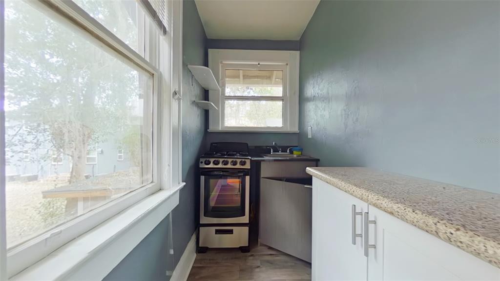 A narrow kitchen features a gas stove, a small sink, and white cabinets with countertops — 1412 NW 3RD AVENUE UNIT Upstairs, GAINESVILLE, FL