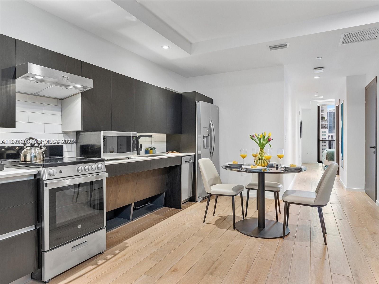 A modern kitchen with dark cabinetry and stainless steel appliances sits beside a small dining area — 398 NE 5th St # 1915, Miami FL 33132, MIAMI, FL