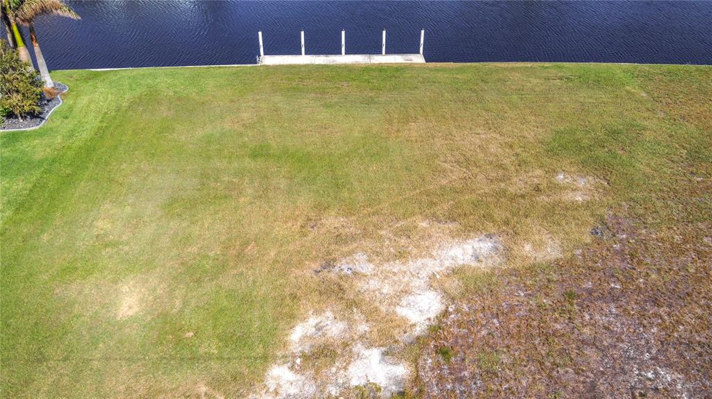An aerial view shows a grassy waterfront lot with a small concrete dock — 3338 SANDPIPER DRIVE, PUNTA GORDA, FL