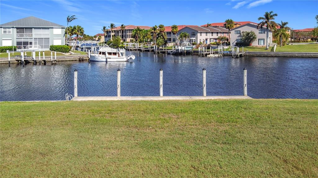 A grassy lawn overlooks a canal with a boat dock and residential buildings in the background — 3338 SANDPIPER DRIVE, PUNTA GORDA, FL