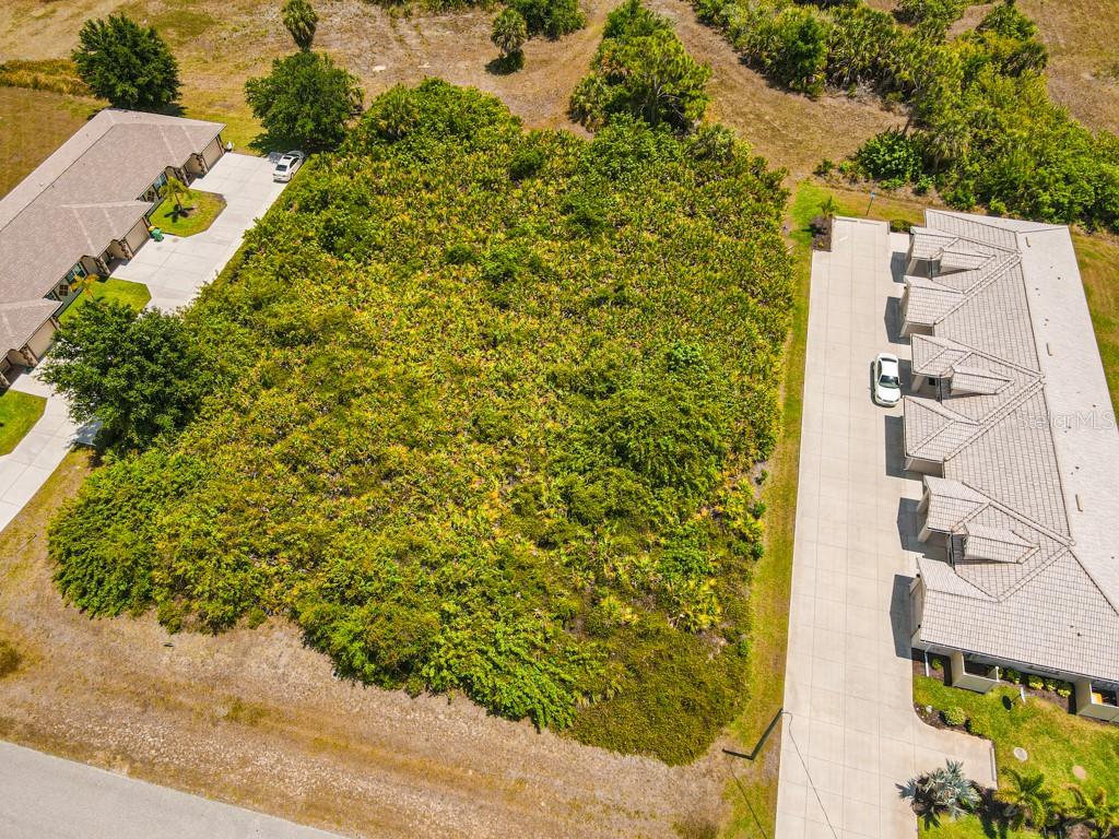 An aerial view shows a vacant, tree-covered lot situated between two residential buildings — 18 DONLON DRIVE, ROTONDA WEST, FL