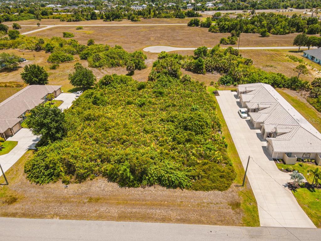 An aerial view shows a vacant, overgrown lot situated between two residential buildings — 18 DONLON DRIVE, ROTONDA WEST, FL