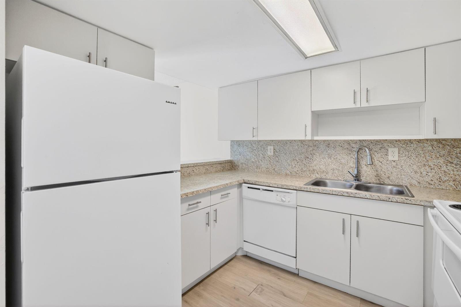 A kitchen features white cabinets, granite countertops, a stainless steel sink, and white appliances — 321 Gulfstream Road, Dania Beach FL 33004, DANIA BEACH, FL