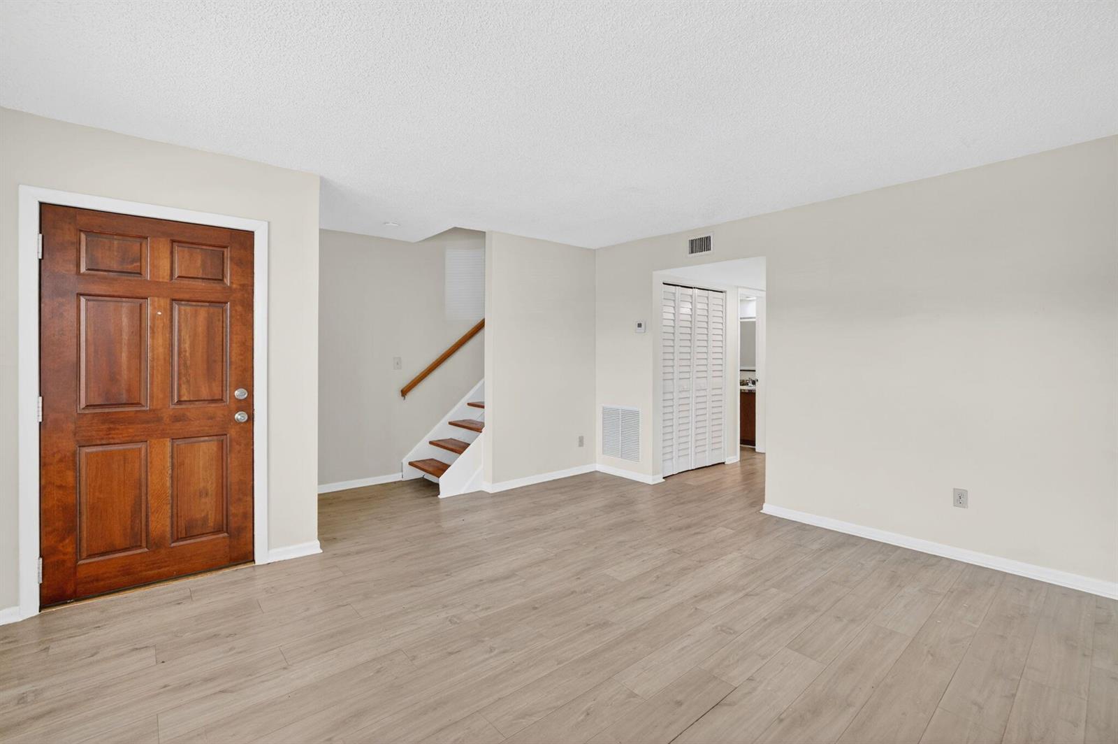 An empty living room features light wood-look flooring, a wooden front door, and a staircase — 321 Gulfstream Road, Dania Beach FL 33004, DANIA BEACH, FL