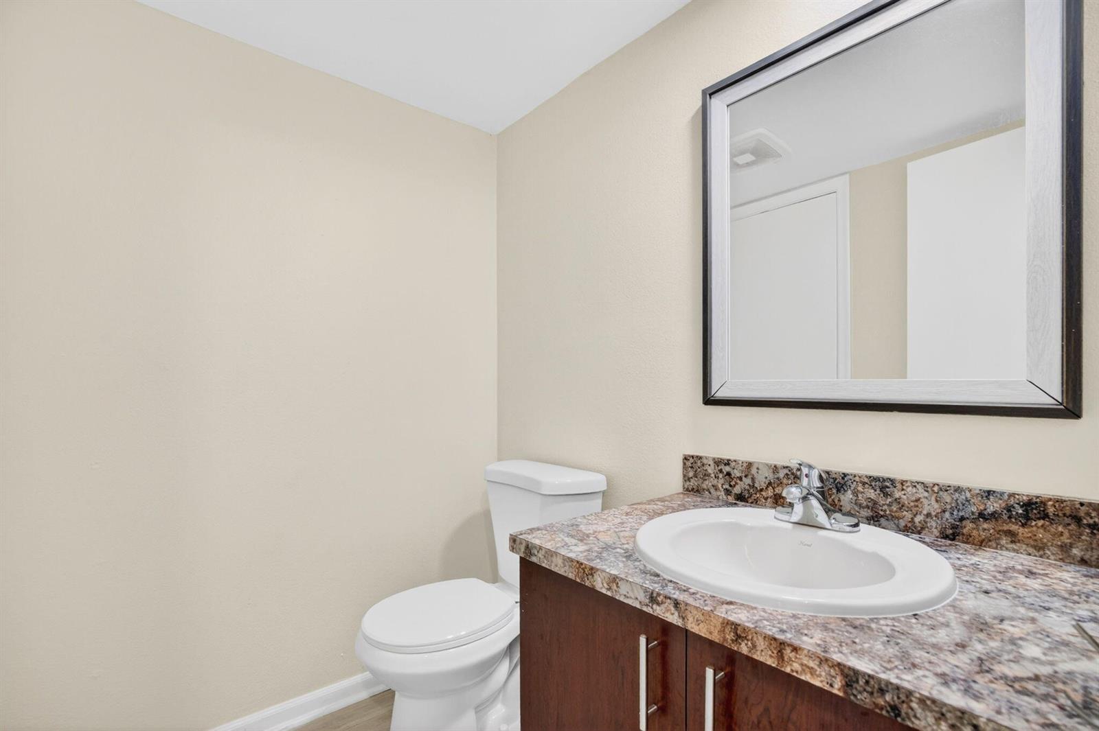 A bathroom features a white toilet, a dark wood vanity with a granite countertop, and a mirror — 321 Gulfstream Road, Dania Beach FL 33004, DANIA BEACH, FL