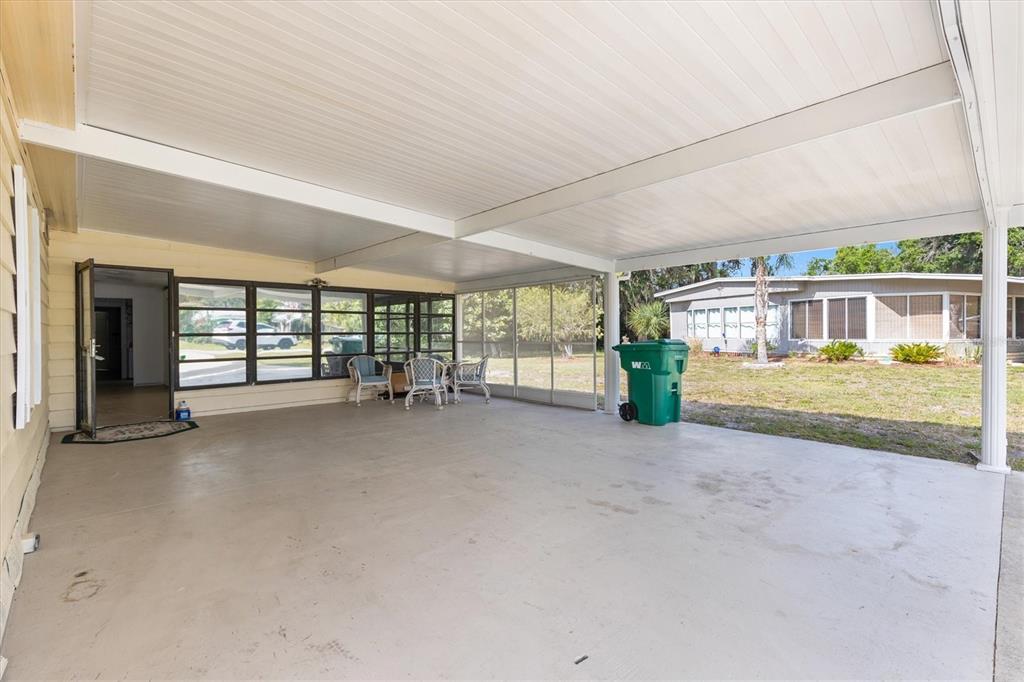 A large concrete patio is covered by a white roof and features a screened enclosure — 5556 COLUMBUS CIRCLE, WILDWOOD, FL