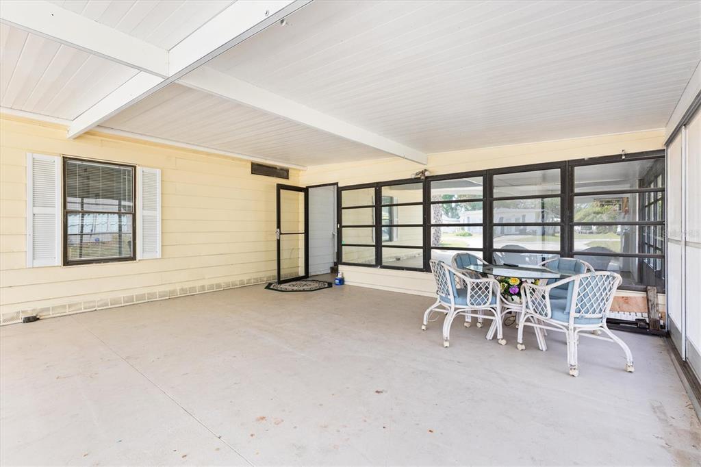 A covered patio with light yellow siding, large windows, and a small dining set — 5556 COLUMBUS CIRCLE, WILDWOOD, FL