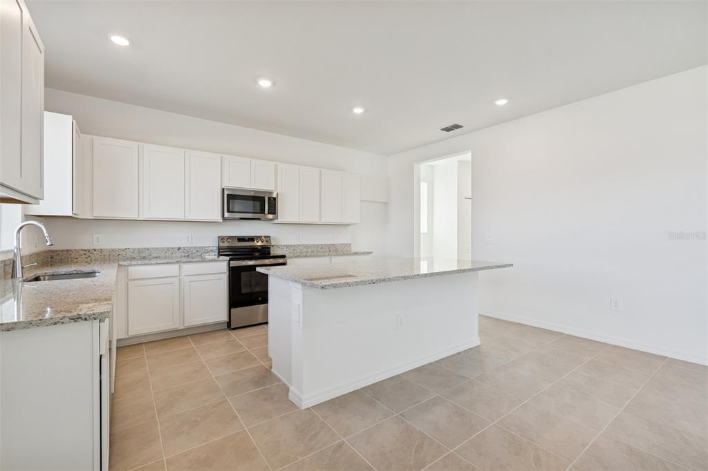 A kitchen features white cabinets, granite countertops, stainless steel appliances, and light tile flooring — 4610 OUTHAUL RUN, PALMETTO, FL