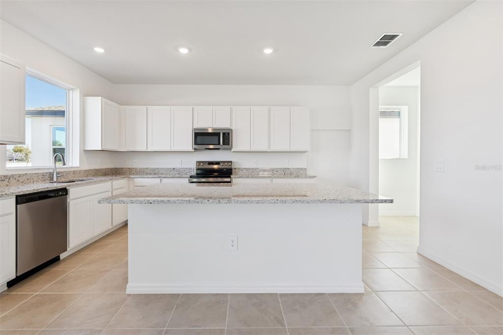 A kitchen features white cabinets, granite countertops, a central island, and stainless steel appliances — 4610 OUTHAUL RUN, PALMETTO, FL