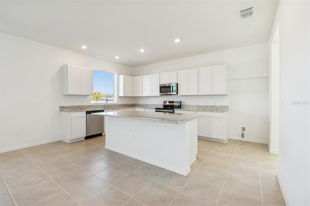 A kitchen with white cabinets, granite countertops, a center island, and light-colored tile flooring — 4610 OUTHAUL RUN, PALMETTO, FL
