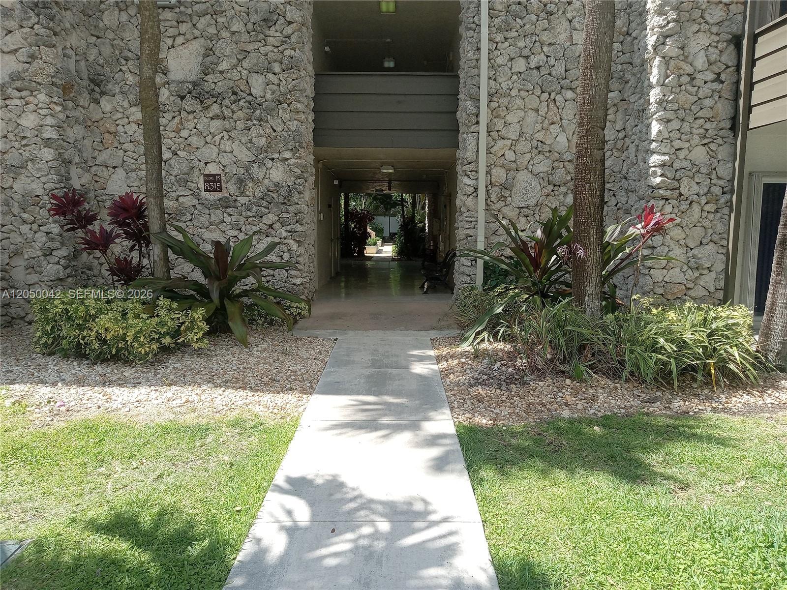 A concrete walkway leads to the entrance of a stone-clad building with tropical landscaping — 8315 SW 72nd Ave # 303B, Miami FL 33143, MIAMI, FL