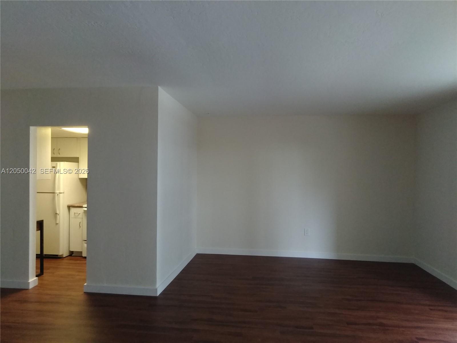 An empty room with dark wood-look flooring and a doorway leading to a kitchen — 8315 SW 72nd Ave # 303B, Miami FL 33143, MIAMI, FL
