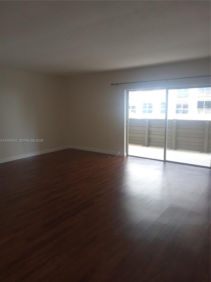 An empty room with dark wood-look flooring and a sliding glass door to a balcony — 8315 SW 72nd Ave # 303B, Miami FL 33143, MIAMI, FL