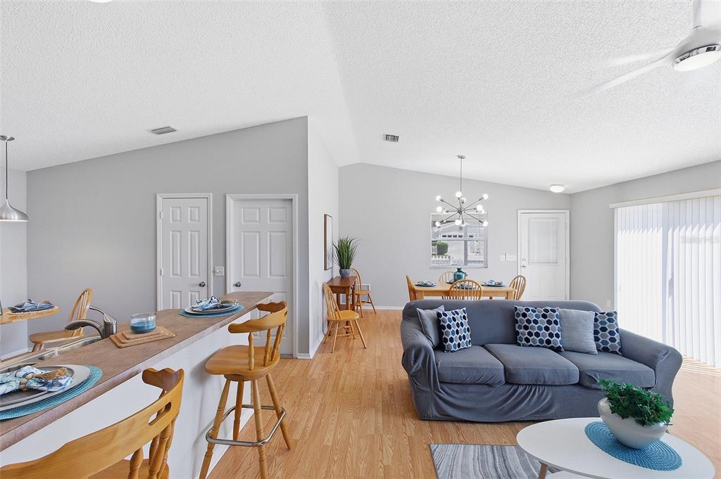 An open-concept living and dining area features light wood flooring, gray walls, and vaulted ceilings — 324 EMMALEE PLACE, THE VILLAGES, FL