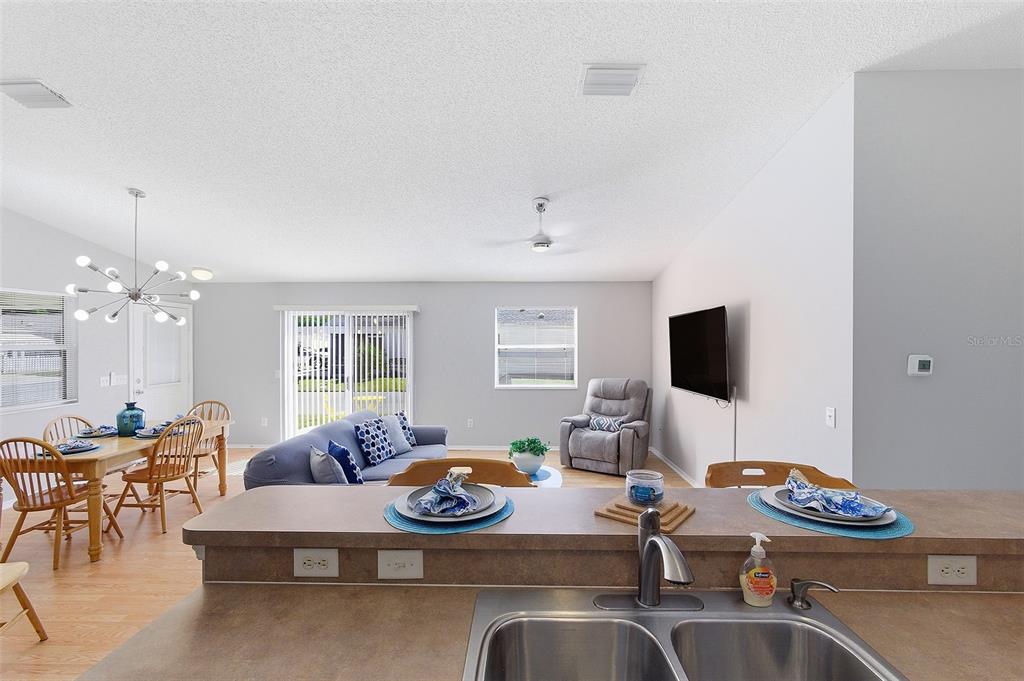 A kitchen island overlooks an open-concept living and dining area with light-colored walls — 324 EMMALEE PLACE, THE VILLAGES, FL