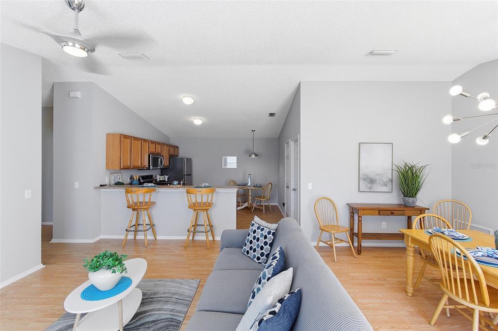 An open-concept living room, dining area, and kitchen with light wood flooring and neutral walls — 324 EMMALEE PLACE, THE VILLAGES, FL