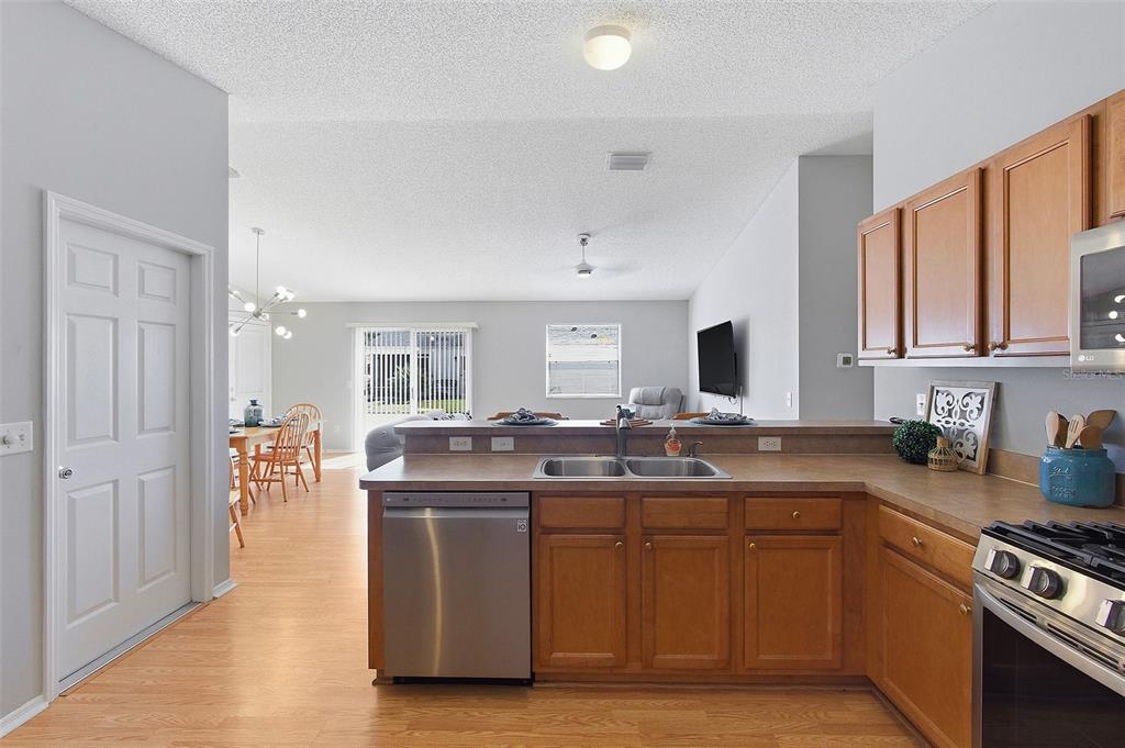 A kitchen with wood cabinets and stainless steel appliances overlooks an open-concept living and dining area — 324 EMMALEE PLACE, THE VILLAGES, FL