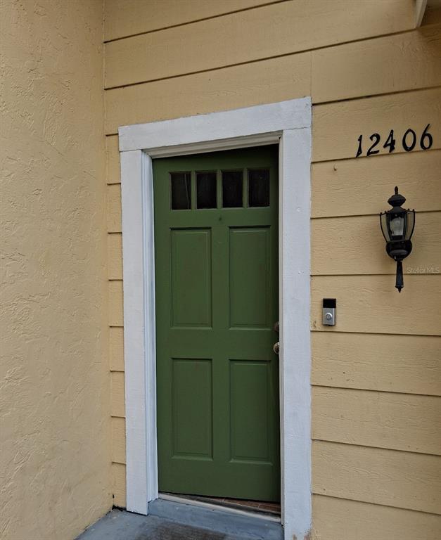 A green four-panel front door with a windowed top sits on a yellow exterior wall — 12406 WEATHERSTONE ROW, HUDSON, FL