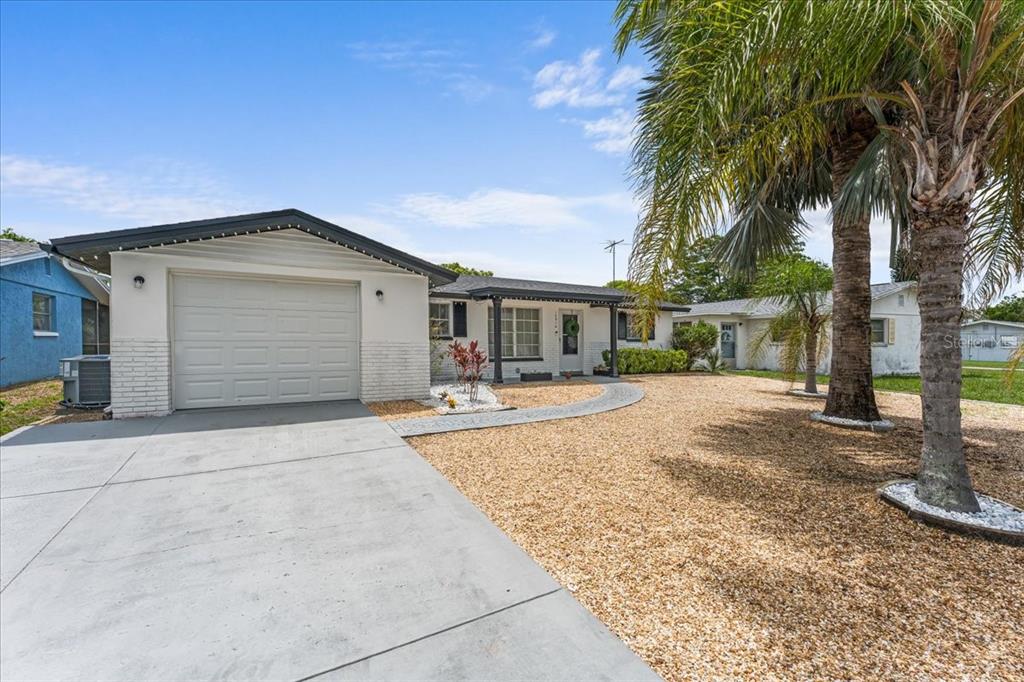 A single-story house with a white exterior, a concrete driveway, and a gravel front yard — 10914 OAKDALE AVENUE, PORT RICHEY, FL