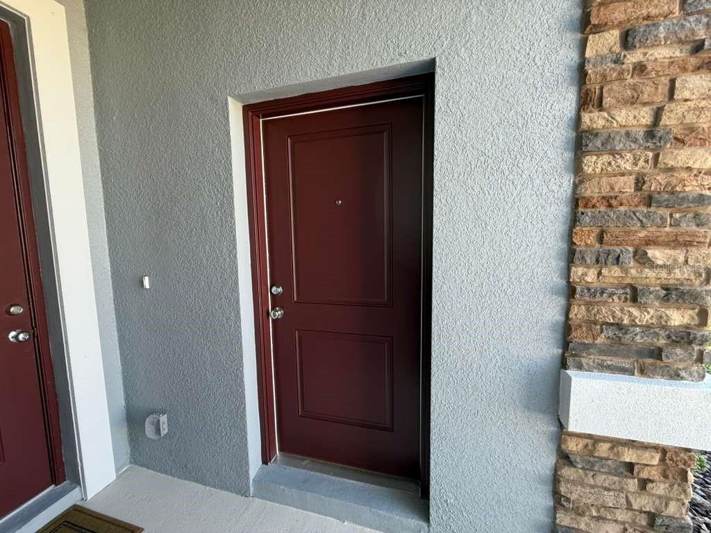 A dark red front door is set into a gray stucco wall next to stone siding — 3483 MUD CANYON DRIVE UNIT A, DAVENPORT, FL