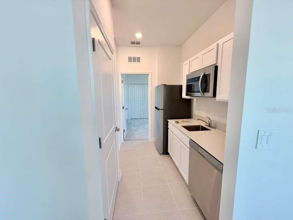 A galley-style kitchen features white cabinets, stainless steel appliances, and light-colored tile flooring — 3483 MUD CANYON DRIVE UNIT A, DAVENPORT, FL