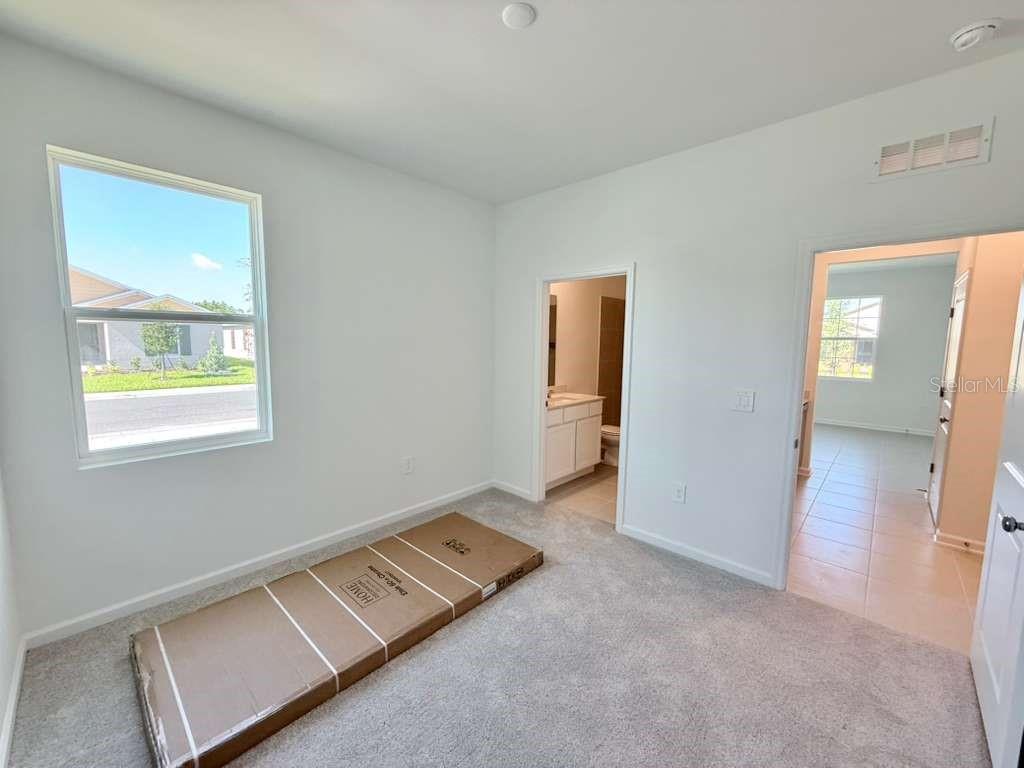 A carpeted bedroom with a window, an attached bathroom, and a large cardboard box — 3483 MUD CANYON DRIVE UNIT A, DAVENPORT, FL