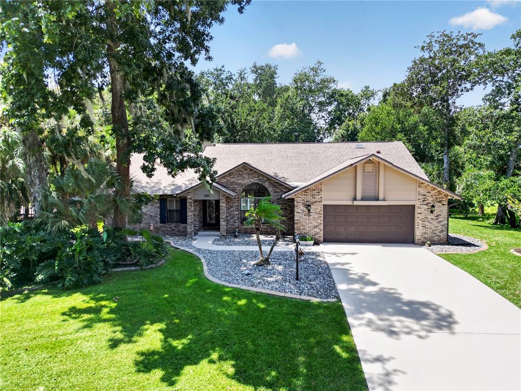 A single-story brick house with a two-car garage, a concrete driveway, and mature trees — 1384 ALEUT LANE, ORMOND BEACH, FL