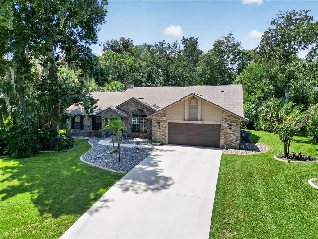 A single-story brick house with a two-car garage, concrete driveway, and surrounding trees — 1384 ALEUT LANE, ORMOND BEACH, FL