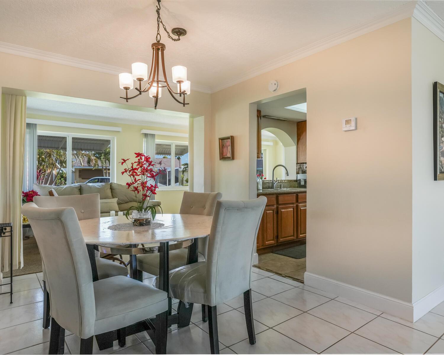 A dining area with a round table, upholstered chairs, and a chandelier, adjacent to a kitchen — 4712 Mainland Drive, Tamarac FL 33319, TAMARAC, FL