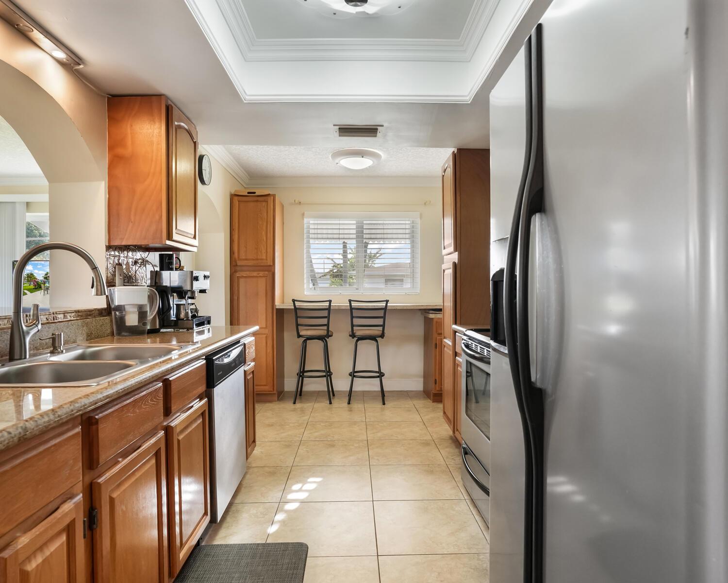A galley kitchen features wood cabinets, granite countertops, stainless steel appliances, and a breakfast bar — 4712 Mainland Drive, Tamarac FL 33319, TAMARAC, FL