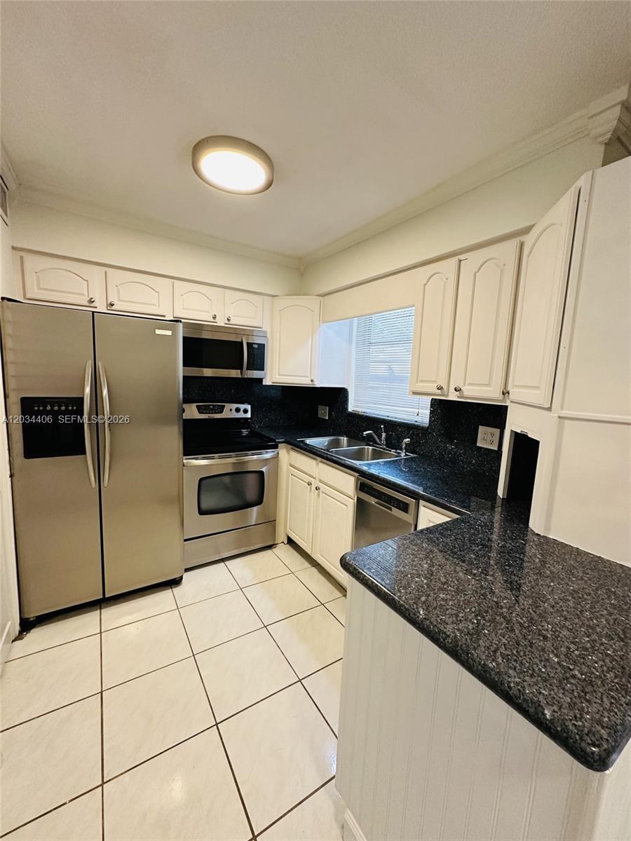 A kitchen features white cabinets, dark granite countertops, stainless steel appliances, and white tile flooring — 2319 Jackson St # 6, Hollywood FL 33020, HOLLYWOOD, FL