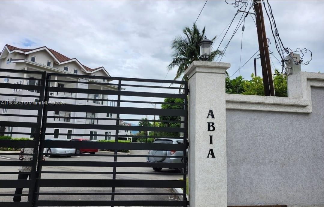 A black metal gate stands before a multi-story building with a parking area — 00 Norbrook, Kingston, Jamaica # 1, NA, NA