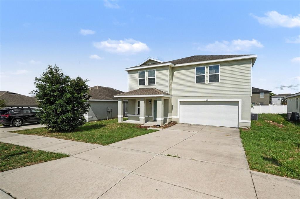 A two-story house with light green siding, a white garage door, and a concrete driveway — 4189 HIGH RIDGE AVENUE, SPRING HILL, FL
